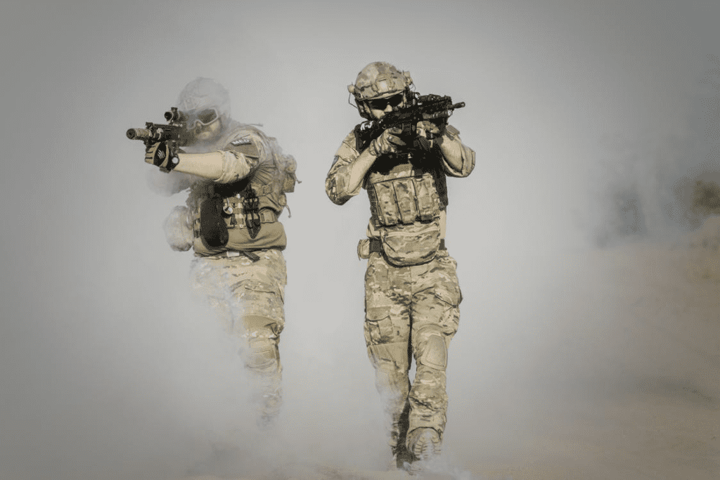 Two solders wearing tactical vests walking through the smoke with rifles in their hands